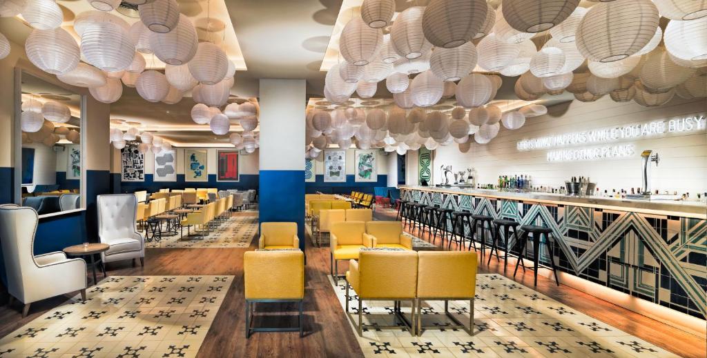 Mūsdienīga bāra interjers ar stilīgu dizainu, kurā ir dzeltenas krēsli un liela bāra letes ar dažādiem dzērieniem. Gaismas ķermeņi no papīra radījuši patīkamu atmosfēru.