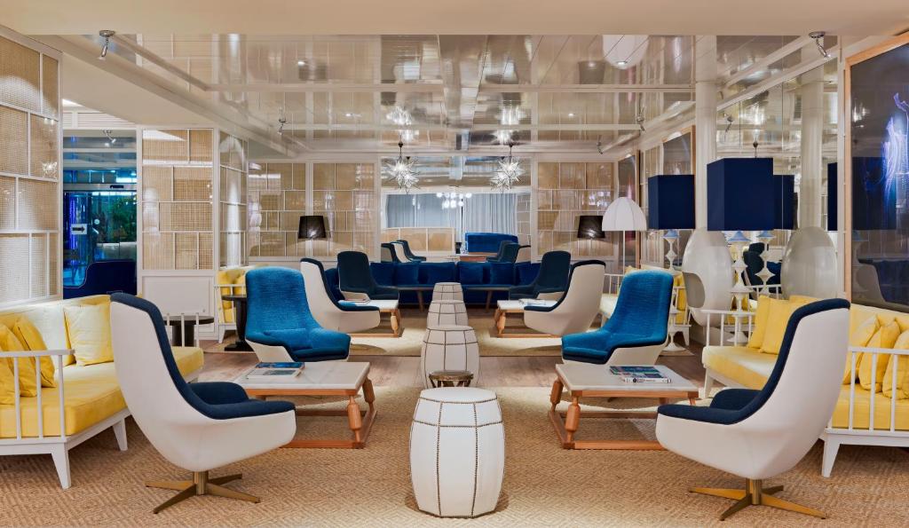 Mūsdienīgs viesnīcas atpūtas zonas interjers ar stilīgām dīvānu grupām un krēsliem, kas apvieno dažādas krāsas un materiālus. Gaismas elementi un atvērts plānojums rada viesmīlīgu atmosfēru.