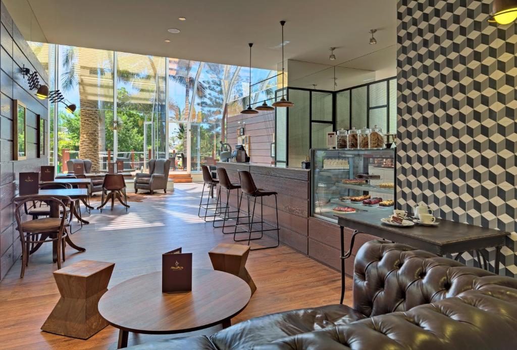 Mūsdienīgs kafejnīcas interjers ar plašiem logiem, koka mēbelēm un ģeometriskām tapetēm, kas rada viesmīlīgu atmosfēru.