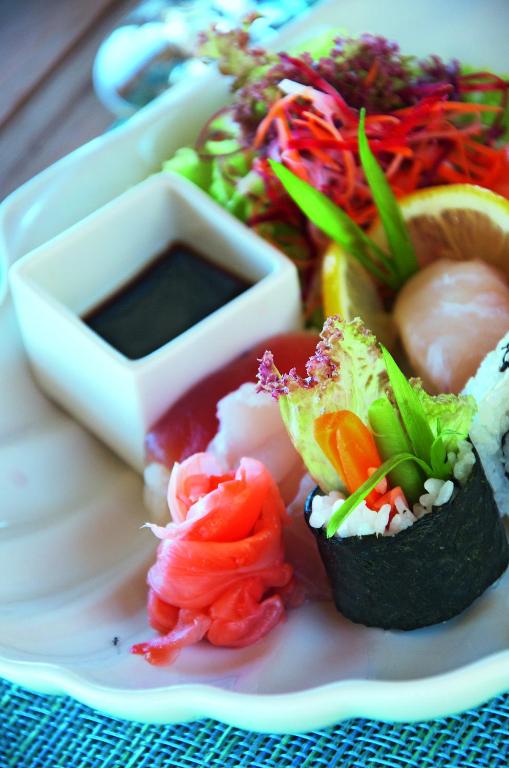 Svaiga sushi šķīvis ar dažādiem suši veidiem, dārzeņiem un sojas mērci, kas pasniegts ar citrona šķēlēm un salātiem.