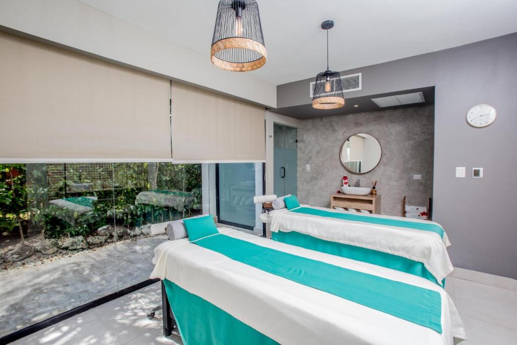 Mūsdienīga spa telpa ar divām masāžas galdiem, kas dekorēti ar zaļiem un baltajiem palagiem. Telpa ir izgaismota ar stilīgām lampām, un caur stikla sienu ir redzama zaļojoša ainava.