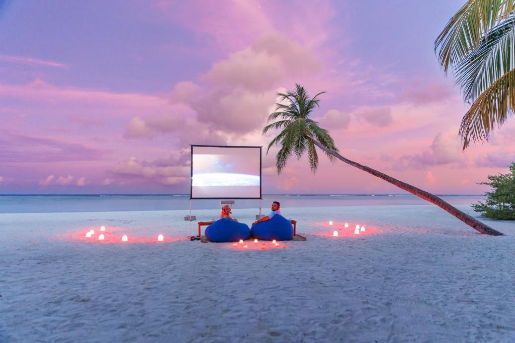 Pludmales kino pieredze ar sēdekļiem un ekrānu, romantisks fons ar saulrieta debesīm un palmām.