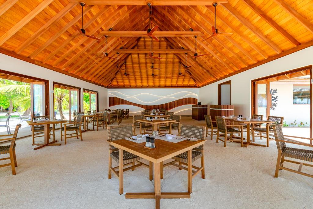 Mūsdienīgs restorāns ar koka griestiem un plašām logu ailēm, kas nodrošina skatu uz dabu. Galdi ir eleganti noformēti ar salvetēm un galda piederumiem, radot patīkamu atmosfēru.