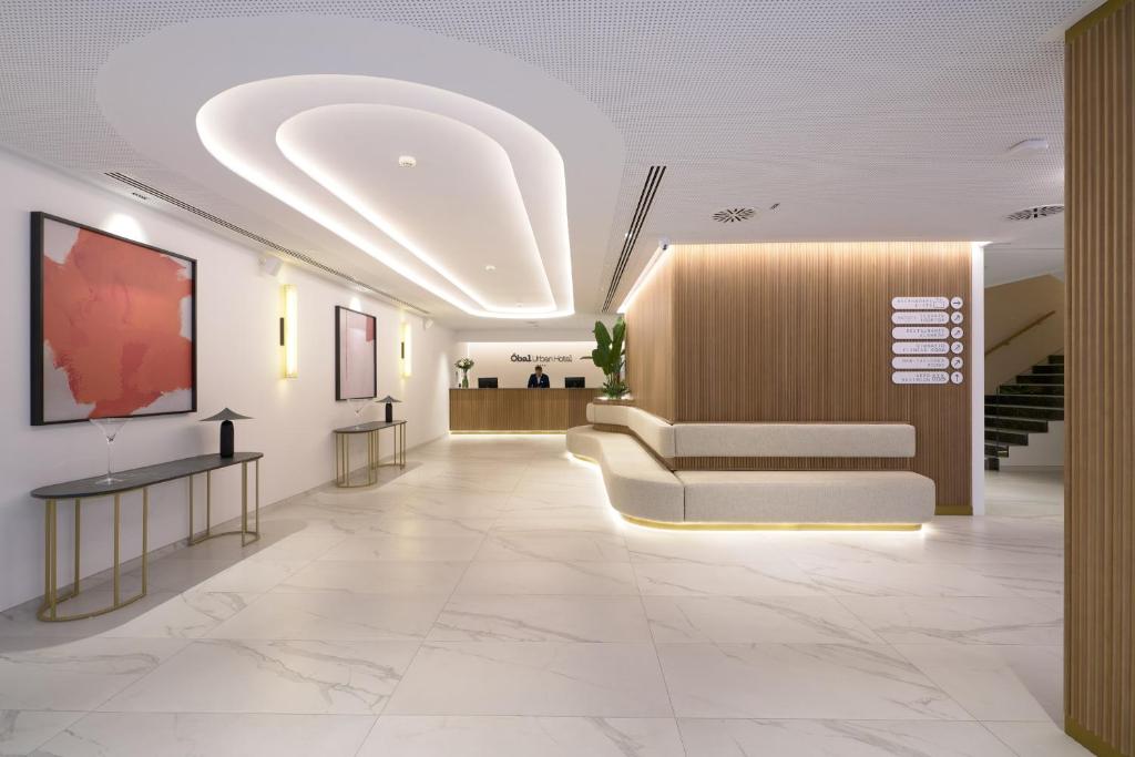 Mūsdienīga viesnīcas recepcija ar elegantu dizainu, kas ietver mākslas darbus un mīkstus apgaismojumus. Telpa ir plaša un gaiša, radot viesmīlīgu atmosfēru.