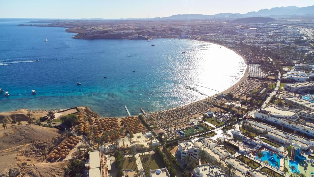 Apskatāms skaists piejūras skats ar zilo jūru, pludmali un viesnīcu kompleksiem, kas izvietoti blakus palmām. Jūras krasts veido pusapli, radot gleznainu ainavu.