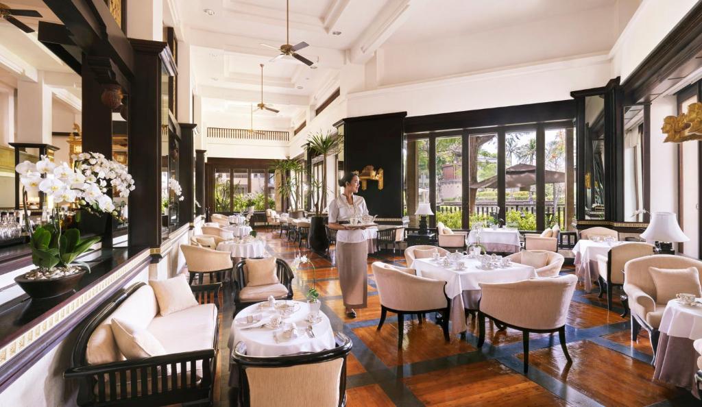 Elegants restorāns ar gaišām telpām un stilu, kurā redzami ziedi un sulīgas augu kompozīcijas. Apkalpotājs stāv pie galda, gatavojoties apkalpot viesus.