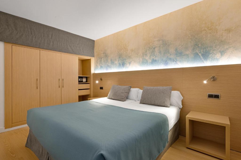 Moderns guļamistabas interjers ar gultu, divām spilveniem un zilu sega. Fona sienā ir stilizēts dekors, un telpā ir koka mēbeles.