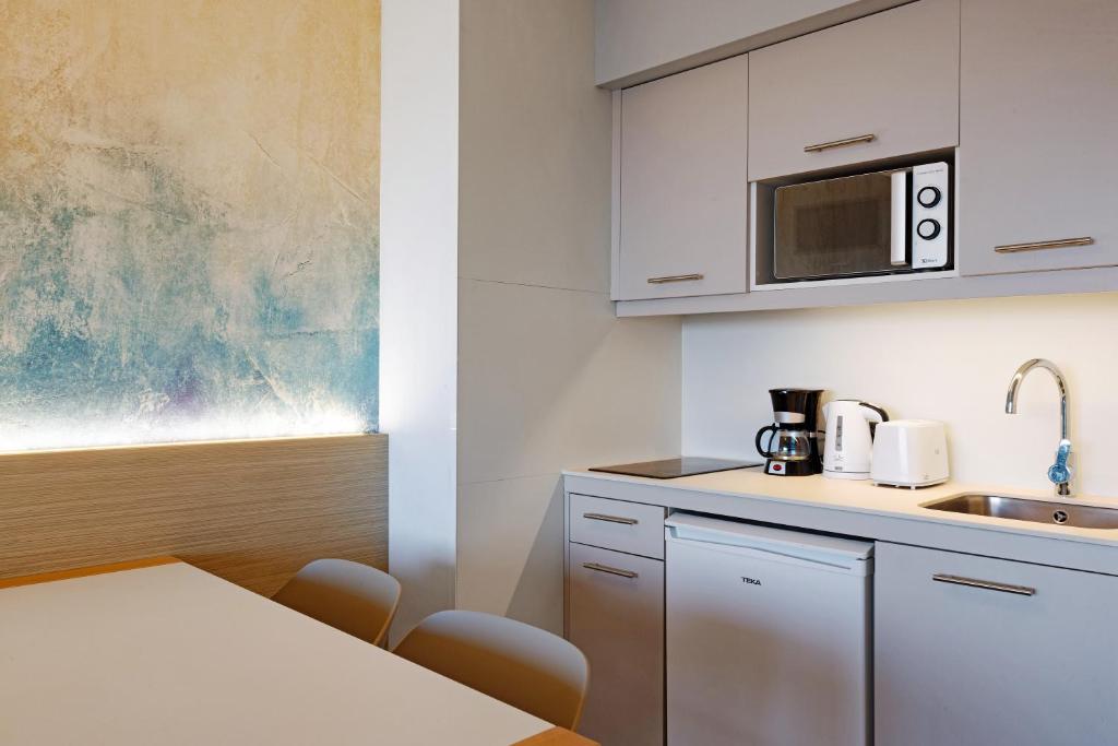 Mūsdienīga virtuve ar pelēkām skapīša durvīm, mikroviļņu krāsni, kafijas automātu un ūdens sildītāju. Gaiša, vienkārša estētika un harmoniska krāsu palete.
