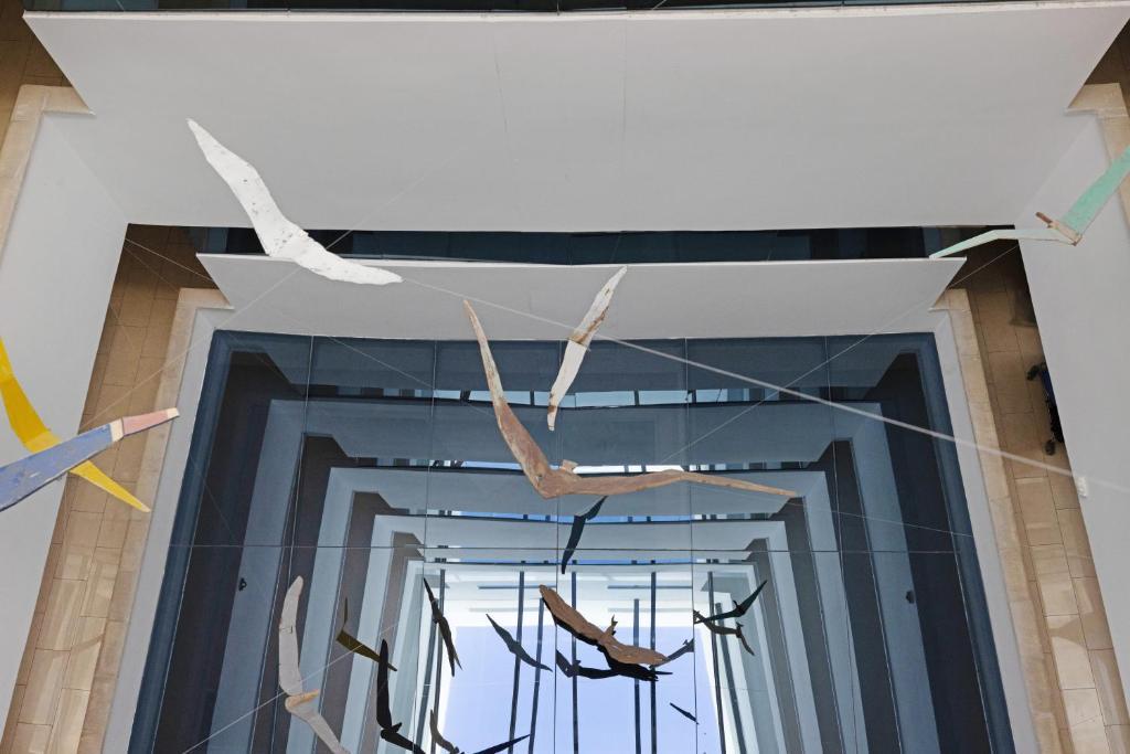 Mūsdienīga mākslas instalācija ar stilizētiem putnu attēliem, kas karājas virs stikla struktūras. Kustības un gaismas spēle rada unikālu estētiku.