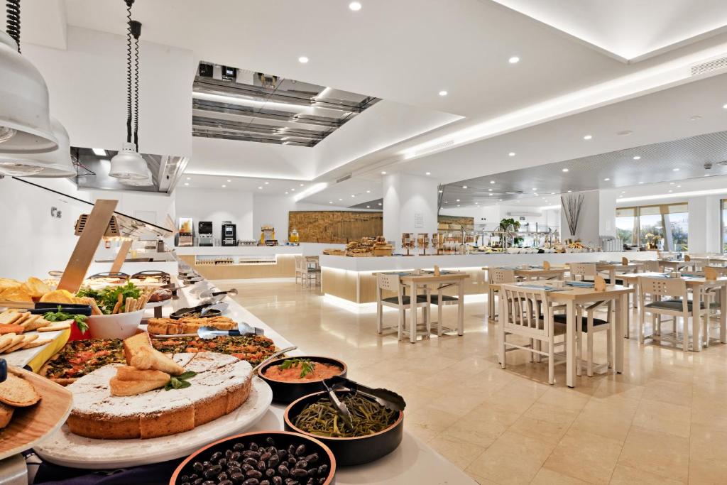 Mūsdienīga restorāna iekšiene ar plašu bufeti, kas piedāvā dažādus ēdienus un saldumus, kopā ar gaišām, minimālistiskām mēbelēm. Ievērojams apgaismojums un atvērtā telpa rada viesmīlīgu atmosfēru.