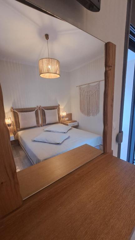 Guļamistaba ar koka mēbelēm un modernu apgaismojumu, atspoguļota spogulī. Interjers ir gaišs un mājīgs, ar dekoratīvām detaļām.