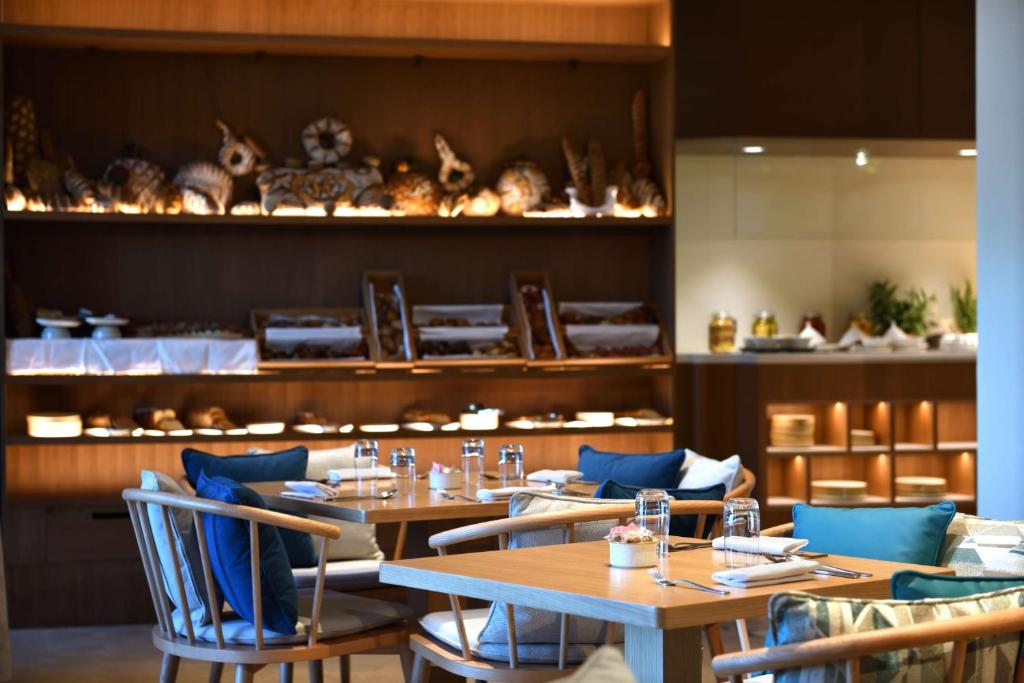 Mūsdienīgs restorāns ar koka mēbelēm un elegantiem galdnieku izstrādājumiem, kas izceļ gardumus uz plauktiem. Silta atmosfēra un uzmanības centrā ir aplūkojami izsmalcināti ēdieni.