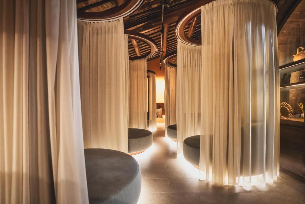 Mūsdienīgs relaksācijas telpas interjers ar mīkstiem sēdekļiem un gaisīgām aizkariem, radot mierīgu atmosfēru. Telpa ir apgaismota ar siltu gaismu, piešķirot intīmu noskaņu.