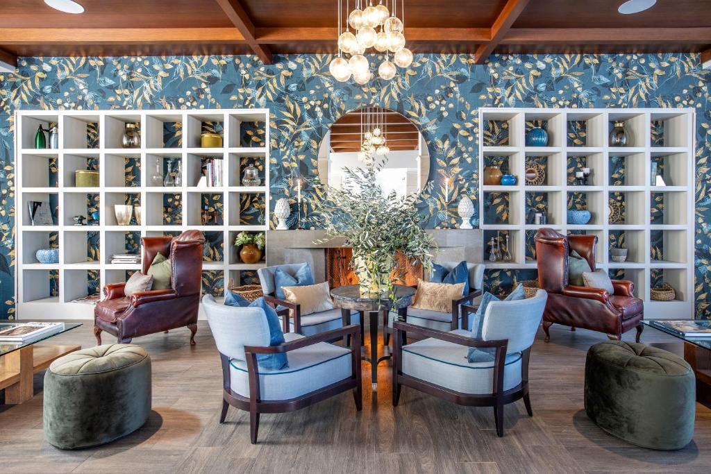 Mūsdienīgs viesistabas interjers ar ziedu tapetēm, elegantiem krēsliem un stilīgu apgaismojumu. Šajā telpā ir plaša grāmatu plaukts un dekoratīvi elementi, kas rada siltu un mājīgu atmosfēru.