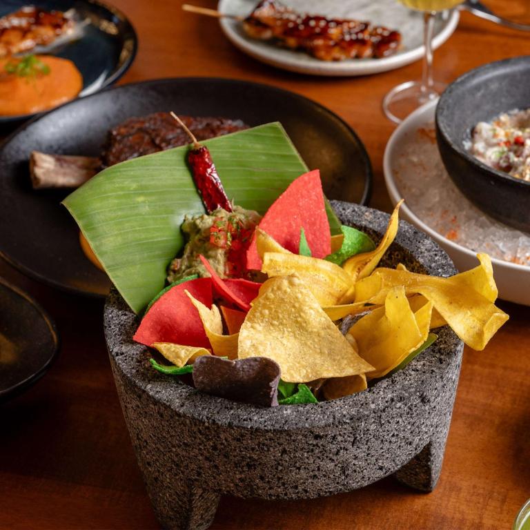 Maltīte ar dažādām čipsu krāsām, pasniegta akmens traukā kopā ar zaļo mērci un dekorēta ar banānu lapām un sarkano čili.