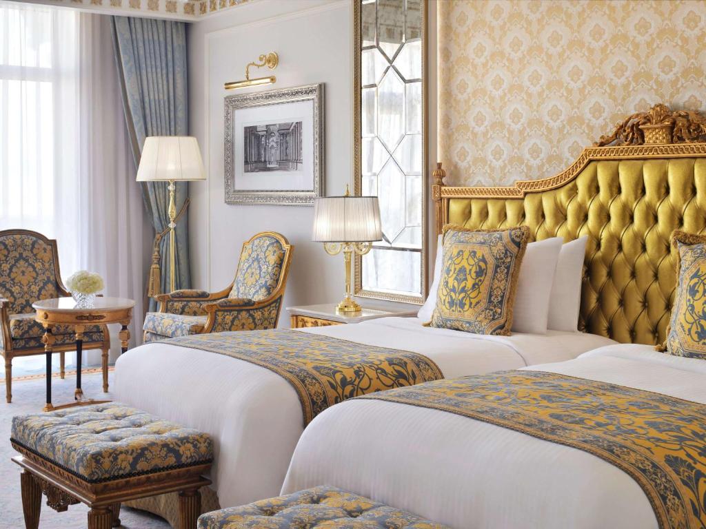 Elegants viesnīcas numurs ar divām gultām, izsmalcinātu dzeltenu galvgali un greznām mēbelēm. Interjers ir dekorēts ar zilo un zelta krāsu akcentiem, radot luksusa atmosfēru.