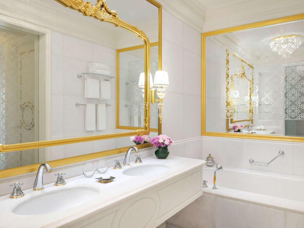 Elegants vannas istabas interjers ar zeltītām spoguļu apmalēm un greznu izlietni, papildināts ar puķu kompozīciju.