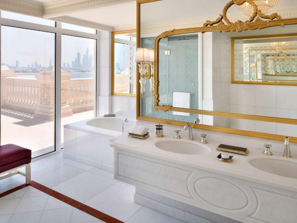 Luksusa vannas istaba ar lieliem logiem, kas piedāvā skatu uz pilsētu, un elegantu spoguli ar zelta rāmi. Modernas iekārtas un harmoniska krāsu palete rada relaksējošu atmosfēru.