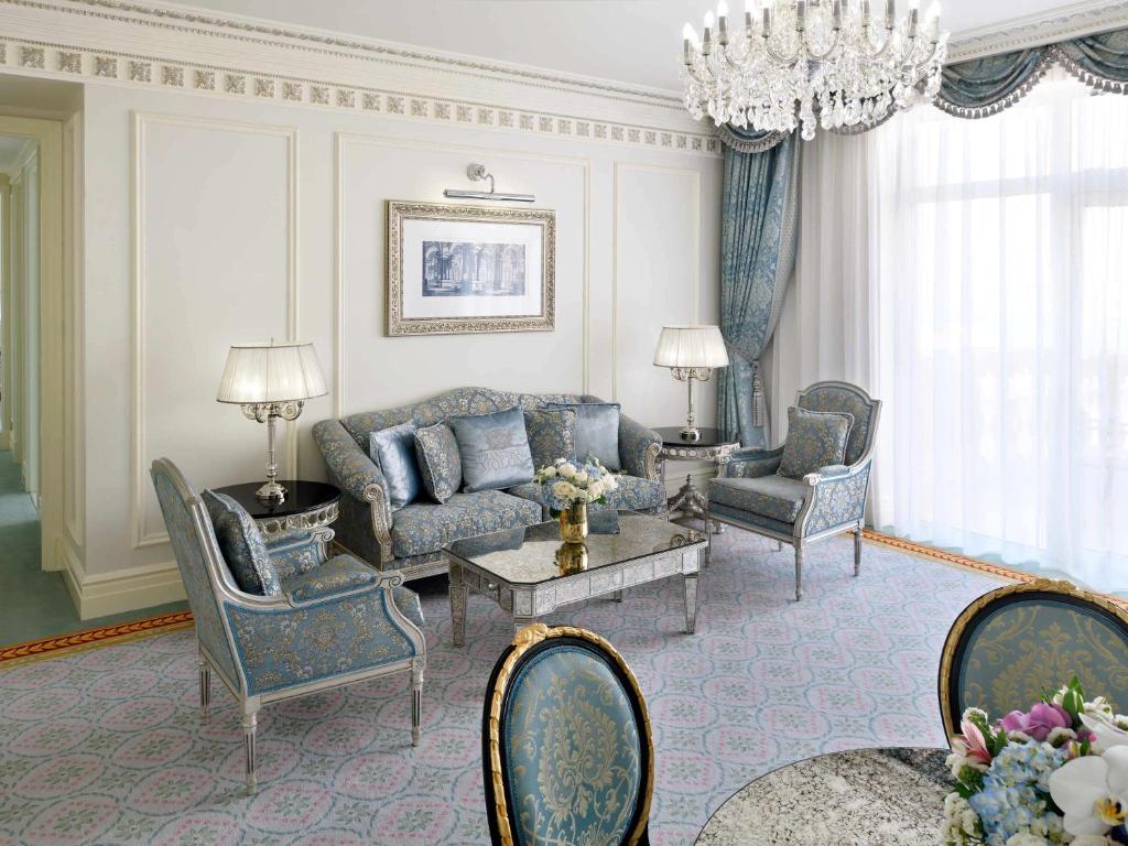 Elegants viesistabas interjers ar zilu un sudraba tonī veidotu mēbeļu komplektu, greznu lustru un gaisīgām aizkariem, kas rada mājīgu atmosfēru. Stūra galds rotāts ar ziediem un mākslinieciskām detaļām.