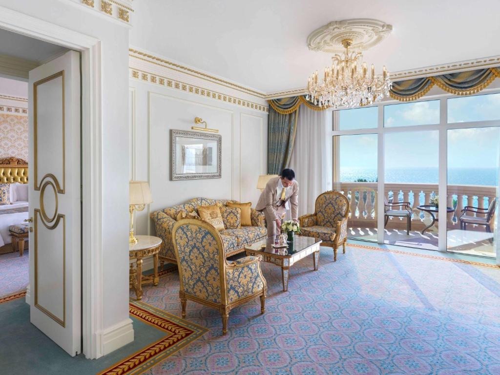 Greznas viesnīcas numura interjers ar skatu uz jūru, kurā redzams elegants dīvāns un krēsli, kā arī lustra. Ideāli piemērots luksusa ceļojumiem.
