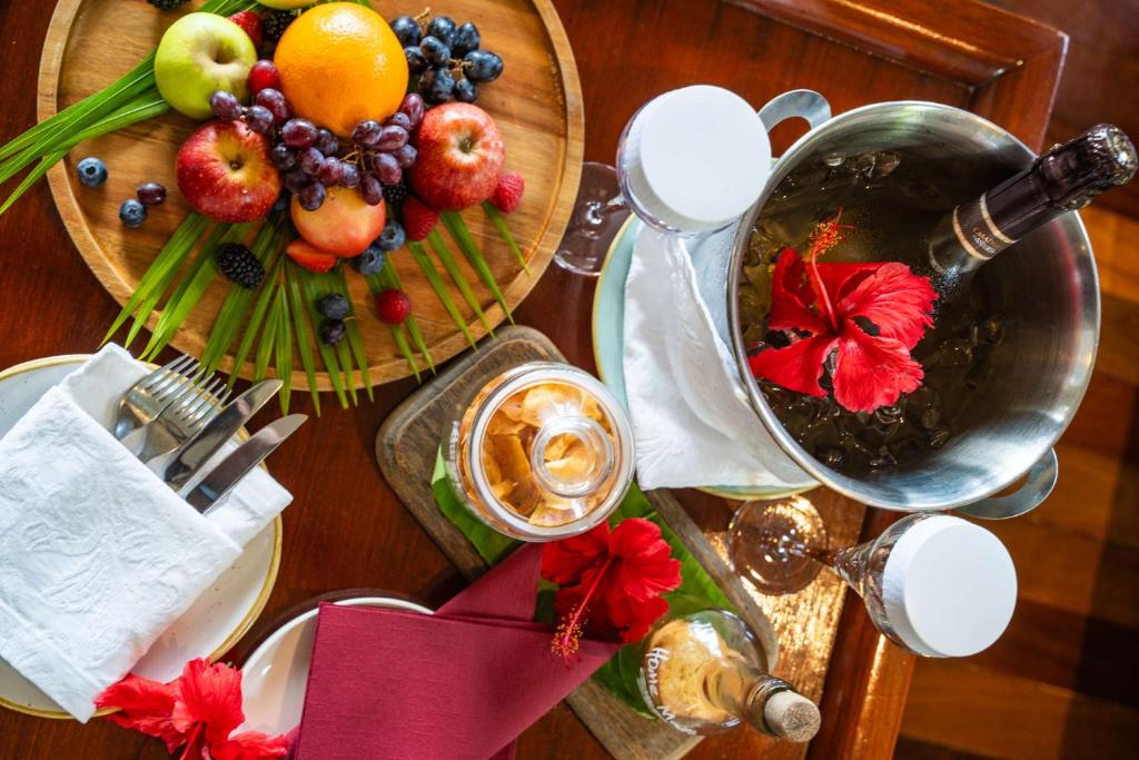 Augļu plate ar āboliem, apelsīniem un ogām, kopā ar dzērienu un ziediem, nodrošina svinīgu atmosfēru. Galda piederumi un dekorācijas pievieno eleganci.