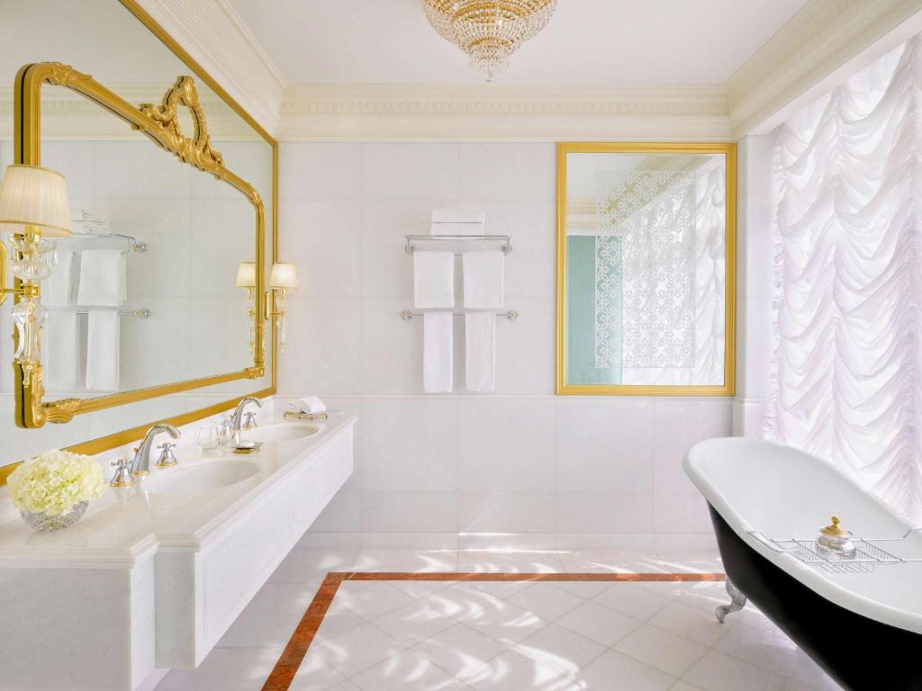 Elegants vannas istabas interjers ar melnu vannu, diviem izlietnēm un greznu spoguli ar zelta rāmjiem. Dabiska gaisma, kas plūst caur logu, uzsver telpas stilīgo dizainu.