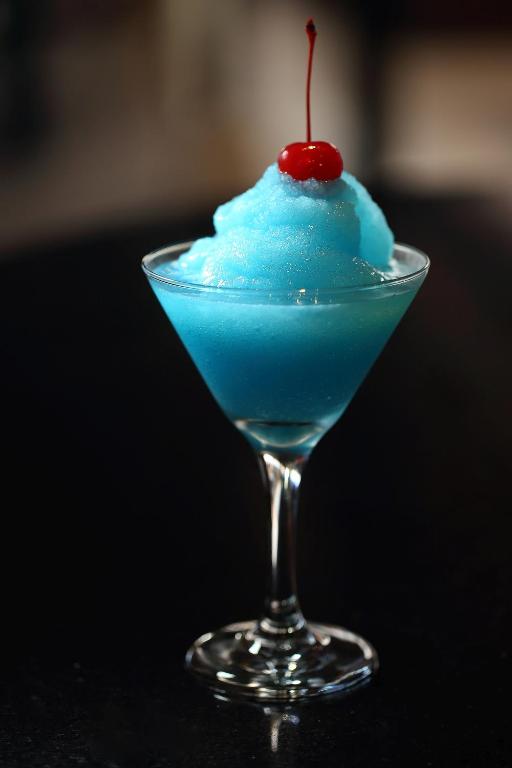 Salds, gaiši zils kokteilis martini glāzē ar zemeņu ķirsīti virsū.