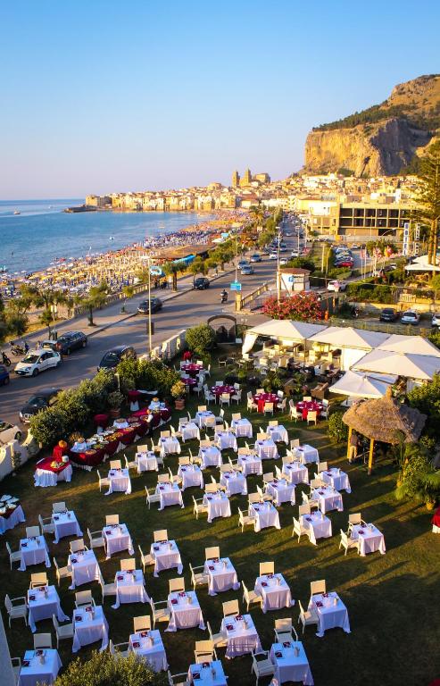 Pludmales restorāna terase ar galdiem, kas izvietoti ārā, un skats uz jūru un pilsētas ainavu.