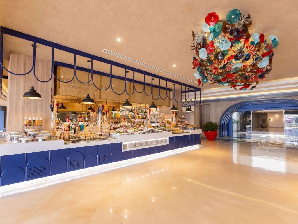 Mūsdienīgs restorāna interjers ar plašu bufeti, dekorētu ar krāsainām rotācijām un modernu apgaismojumu. Gaisā paveras grezna atmosfēra, kas aicina apmeklētājus baudīt maltītes.