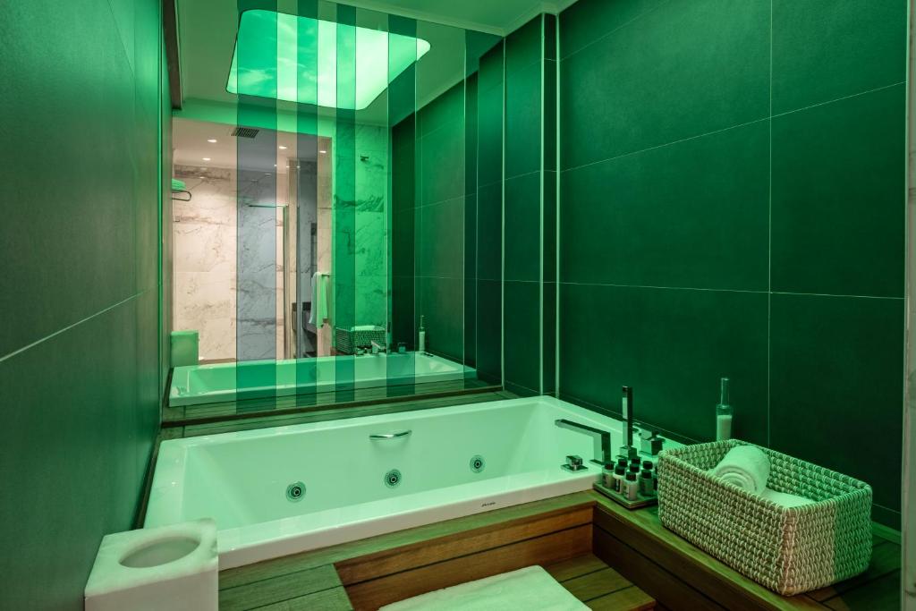 Mūsdienīgs vannas istabas interjers ar zaļām gaismām, kas izceļ vannu un stilīgus aksesuārus. Eleganta un relaksējoša atmosfēra, kas aicina uz atpūtu.