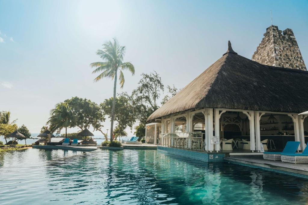 Tropu kūrorts pie baseina ar mājīgu pili un palmām, kas piedāvā ideālu atpūtu saulainā dienā. Skats uz zilu ūdeni un zaļiem kokiem radīs relaksējošu atmosfēru.