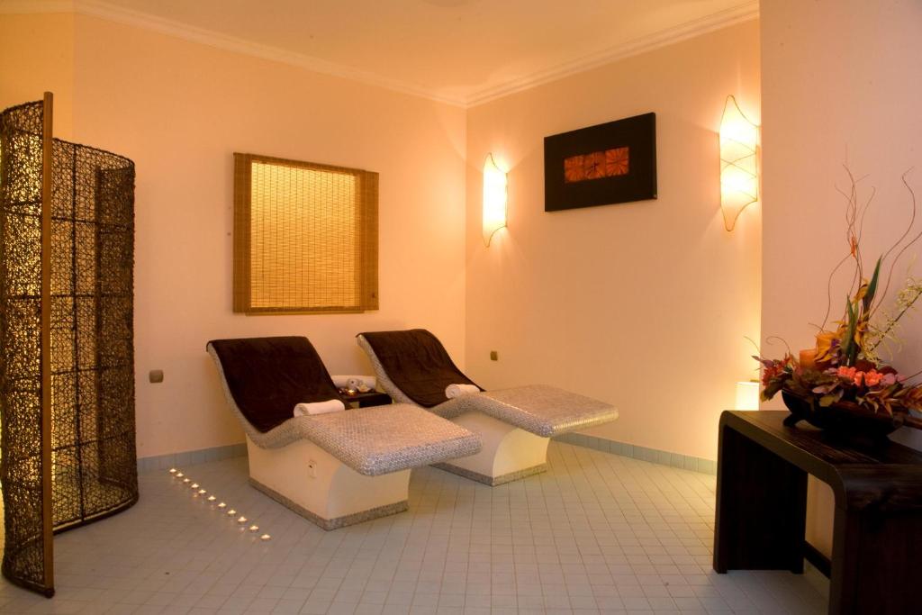 Relaksējoša spa telpa ar divām šūpuļkrēslām un siltu apgaismojumu, kurā ir dekoratīvi elementi un ziedu kompozīcija. Ideāla vieta atpūtai un relaksācijai.