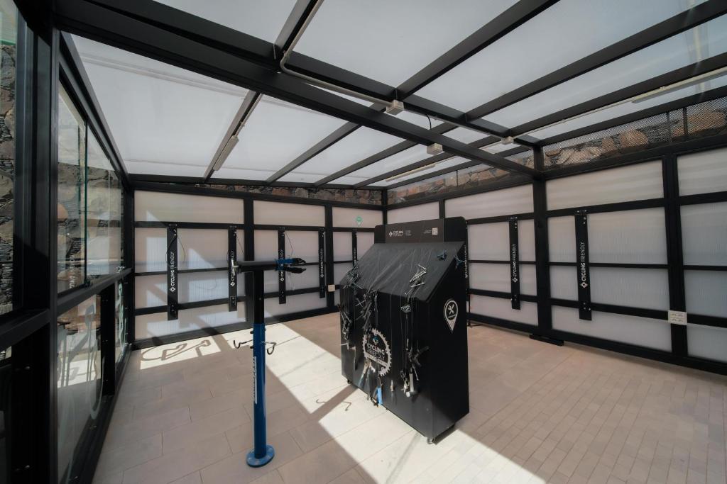 Mūsdienīga telpa ar stiklotām sienām un apgaismojumu, kurā redzams kalnu riteņbraukšanas aprīkojums un sagatavošanās zona. Telpa ir aprīkota ar instrumentiem un aprīkojumu, kas paredzēts riteņu apkopei.