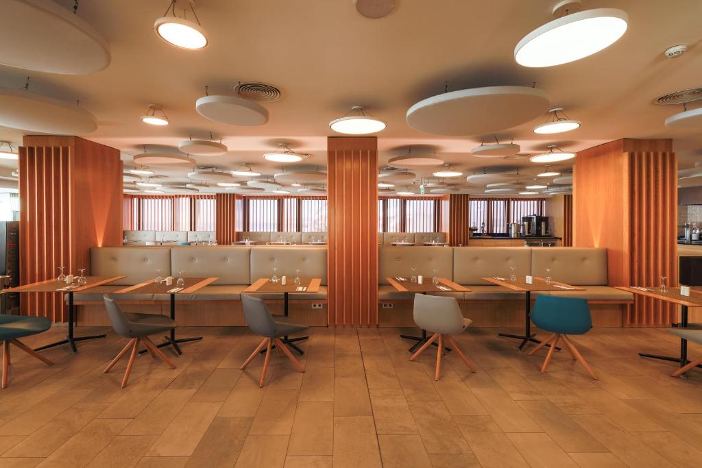 Mūsdienīgs restorāns ar elegantu interjeru, kurā ir koka akcenti un stilīgas krēsli. Gaismas elementi un plašas logu ailes rada patīkamu atmosfēru.