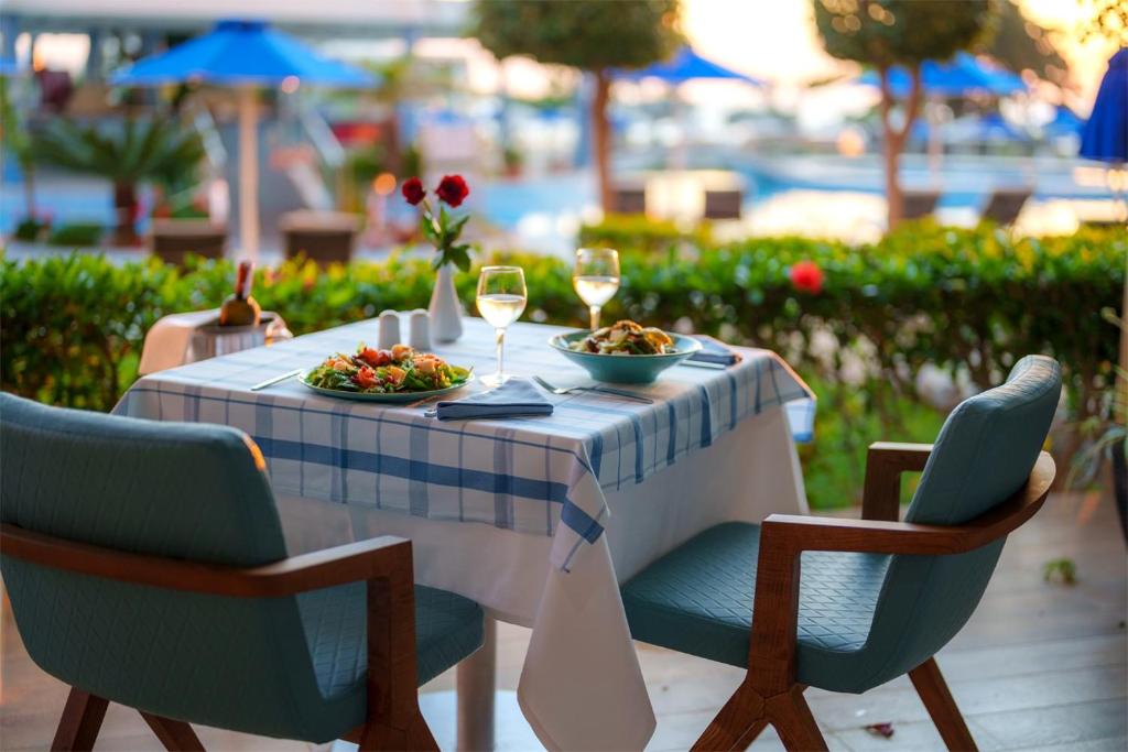 Romantisks galda uzstādījums restorānā ar gardiem ēdieniem un vīna glāzēm, kas atrodas pie peldbaseina. Krāsainas rožu pušķis pie galda papildina atmosfēru.