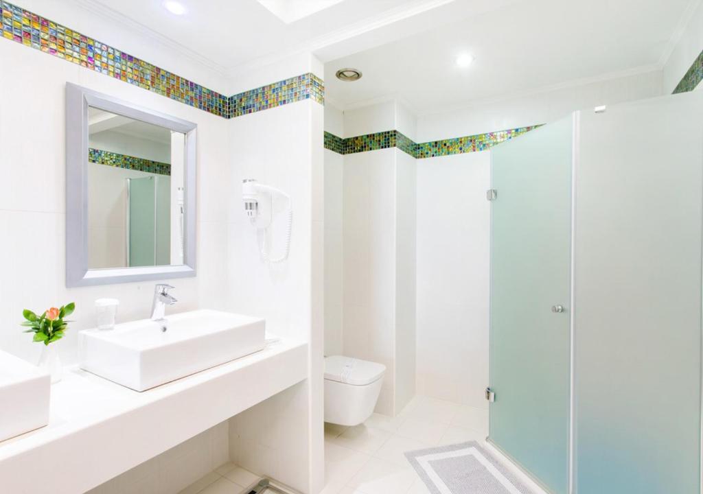 Mūsdienīgs vannas istabas interjers ar gaišām sienām, elegantu izlietni un dušas kabīni, papildināts ar krāsainām mozaīkām un augu dekoru.