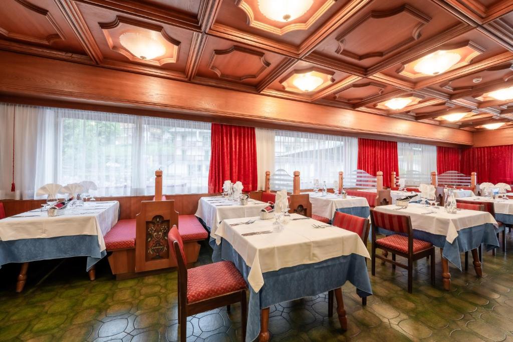 Elegants restorāna interjers ar koka apdari un sarkanām aizkarām, kur galdi ir klāti ar baltām un zilo galdautu. Gaismas no griestiem rada siltu atmosfēru.