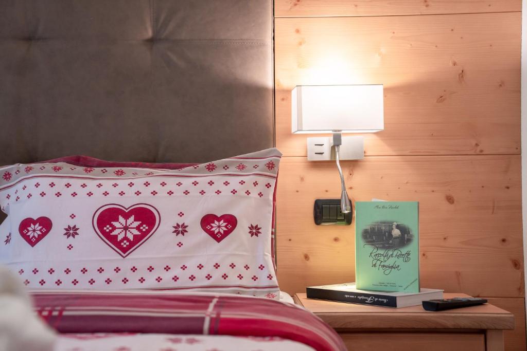 Gultas komplekts ar sirdīm un sniega ziediem, blakus gultai ir nakts lampiņa un grāmata uz naktsgaldiņa, kas radīt mājīgu atmosfēru.