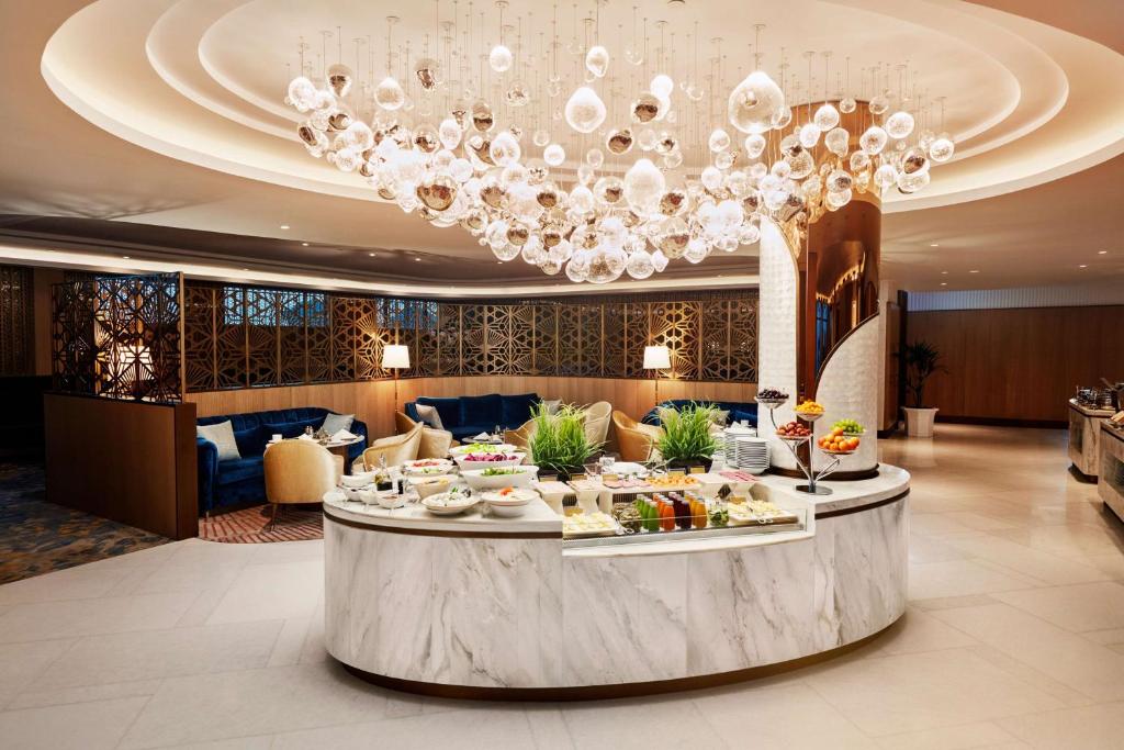 Elegants restorāna interjers ar modernu gaismekli un bufeti, kurā ir dažādi ēdieni un augļi. Svaiga un stilīga atmosfēra, kas aicina apmeklētājus izbaudīt maltīti.