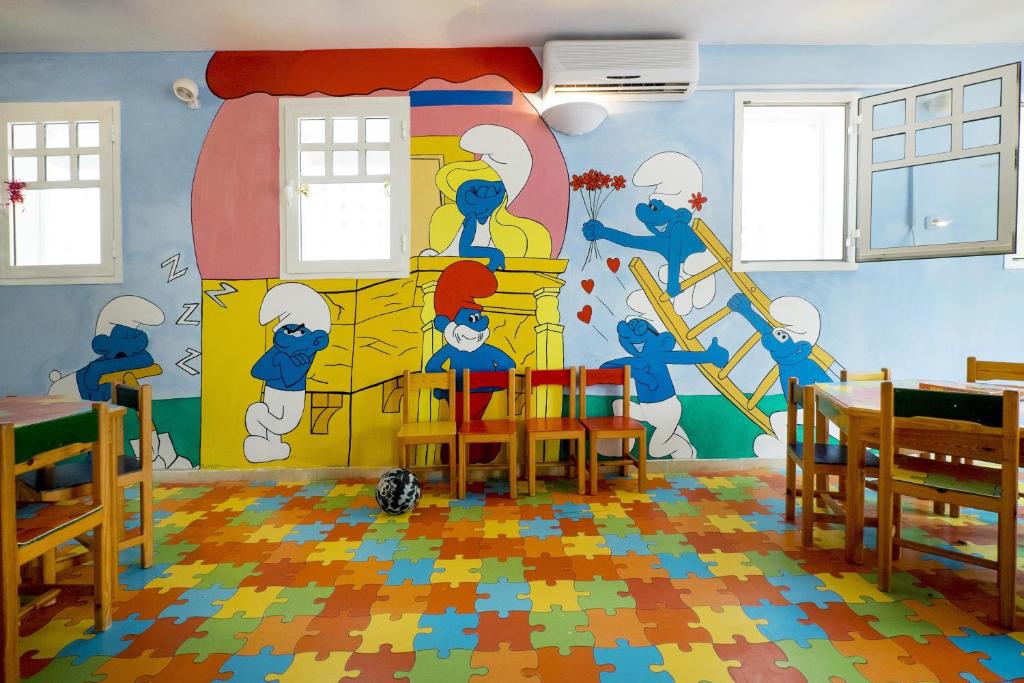 Bērnu istaba ar krāsainiem puzles grīdas segumiem un uz sienām zīmētiem Smurfiem. Telpas interjers ir jautrs un draudzīgs, ideāli piemērots bērniem.