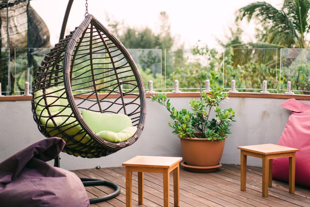 Balkona telpa ar piekārtojušos šūpuļkrēslu, zaļo spilvenu un dekoratīvām augiem. Koka galdiņi un krēsli papildina relaksējošo atmosfēru.