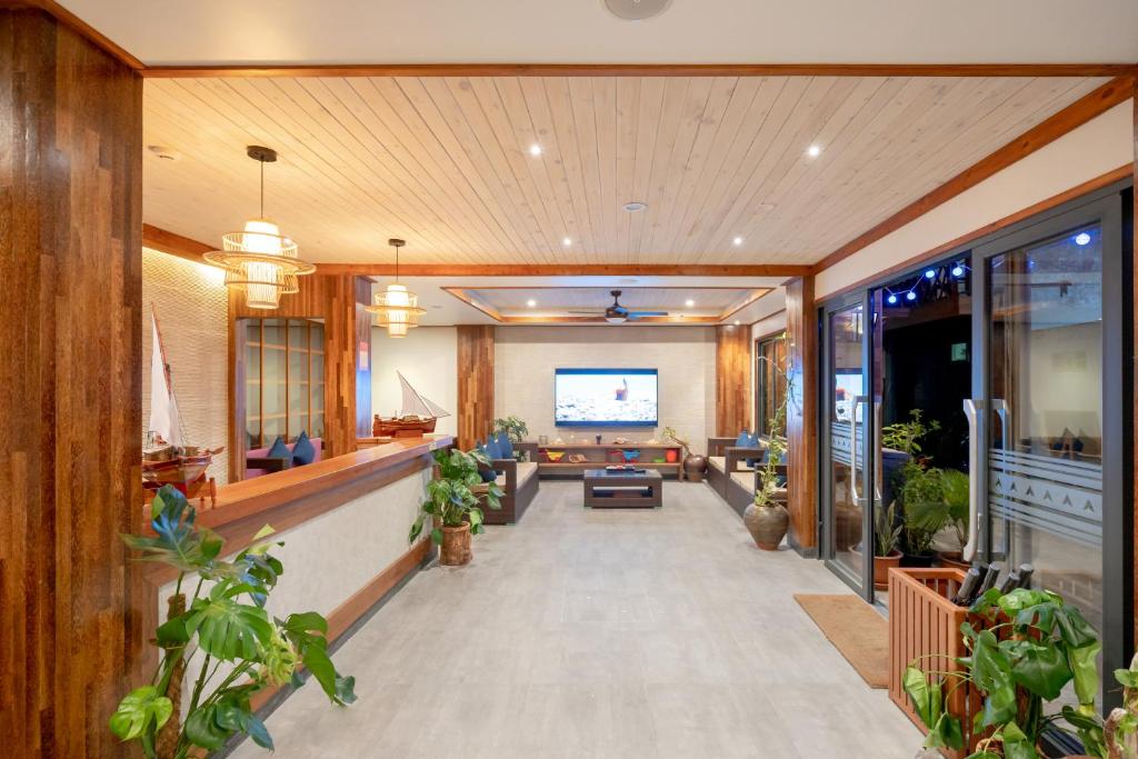 Mūsdienīgs viesnīcas vestibils ar koka apdari, dekoratīvām lampām un zaļiem augiem, radot siltu un viesmīlīgu atmosfēru. Centrā atrodas televizors un sēdvietas relaksācijai.