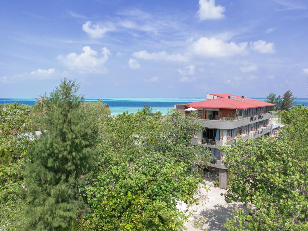 Tropu viesnīca ar sarkanu jumtu, ieskauta zaļiem kokiem un skatu uz zilajiem ūdeņiem. Ideāla vieta relaksācijai un atpūtai.