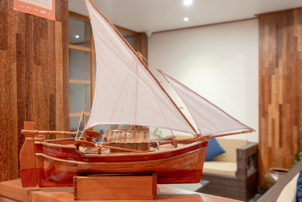 Koka laivas modelis ar baltu buru, izvietots interjerā, ar koka sienām un mīkstiem krēsliem fona.