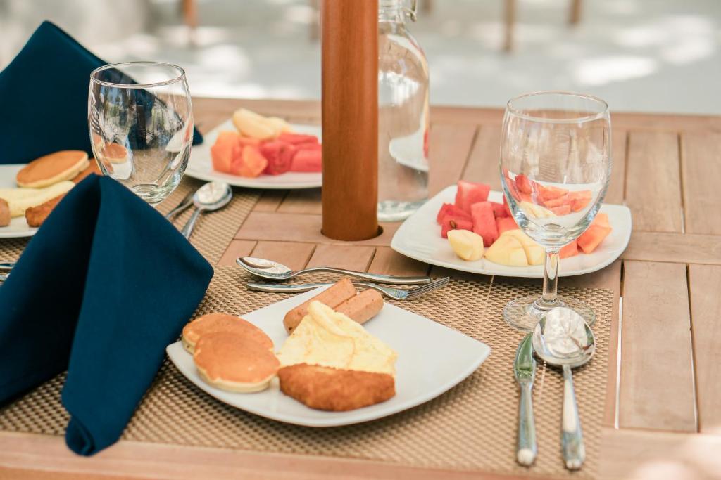 Brokastu galda klājums ar dažādiem ēdieniem, tostarp pankūkām, augļiem un dzērieniem. Galda dekors ir elegants, ar tumšām salvetēm un sudraba galda piederumiem.