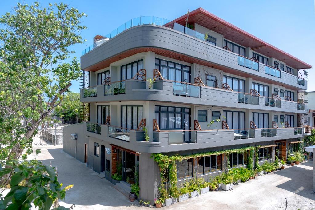 Mūsdienīga viesnīca ar plašām terasēm un zaļiem augiem ap ēku, kas atrodas saulainā vidē.