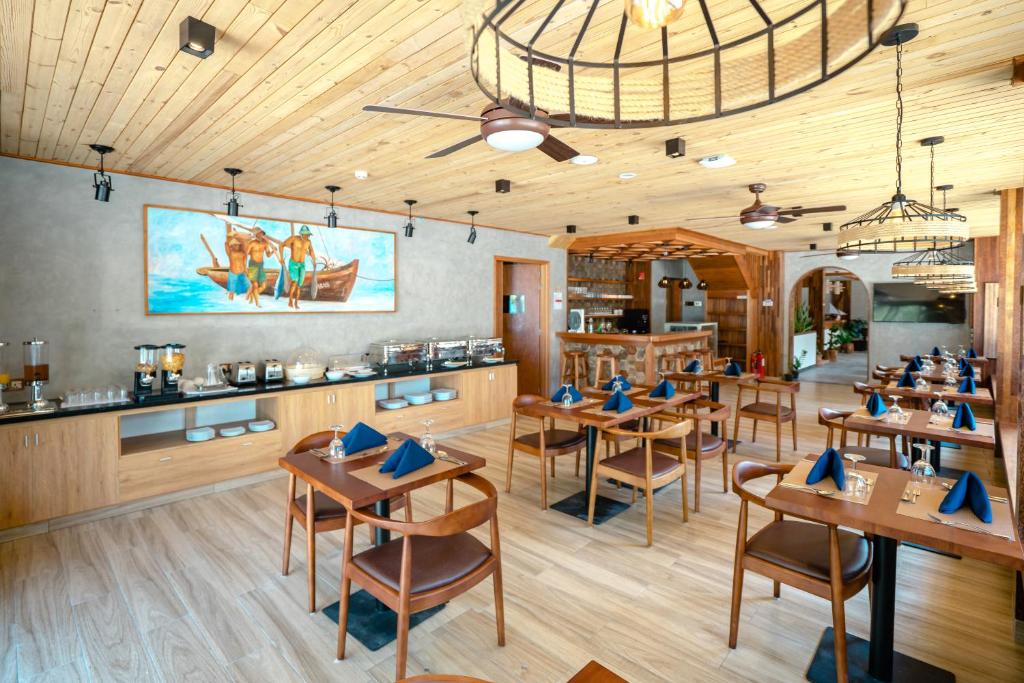 Mūsdienīga restorāna iekārtojums ar koka apdari un mākslas darbu uz sienas. Galdi ir sakārtoti ar ziliem galdautiem un elegantiem galda piederumiem.