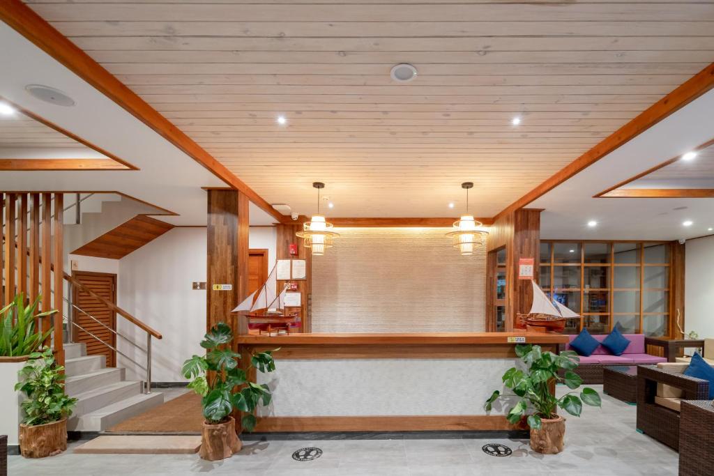 Mūsdienīgs viesnīcas reģistratūras interjers ar koka apdari, dekoratīvām augiem un ērtām sēdvietām. Iekšējā apgaismojuma elementi rada siltu un viesmīlīgu atmosfēru.