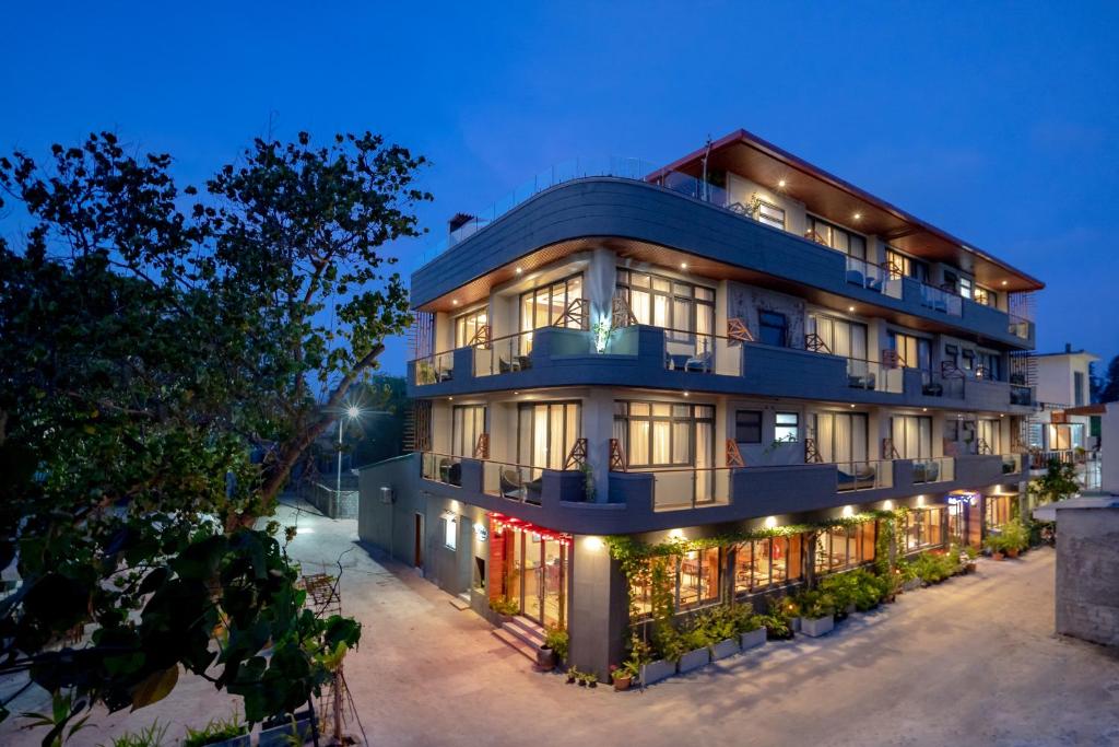 Moderns viesnīcas ēka ar balkoniem, apstādījumiem un izgaismotiem logiem, uzņemta krēslā.