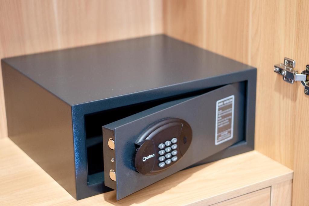 Melns seifs ar ciparu tastatūru, daļēji atvērts un novietots koka skapī. Seifs ir izturīgs un piemērots vērtīgu priekšmetu glabāšanai.